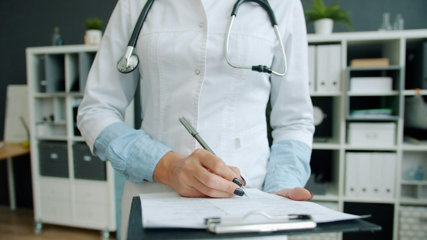 A clinician signing a form on a clipboard